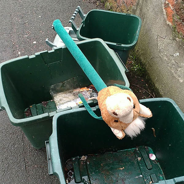 Abandoned, unwanted, unloved, cuddly toy - hobby horse lying across some empty green recycling bins